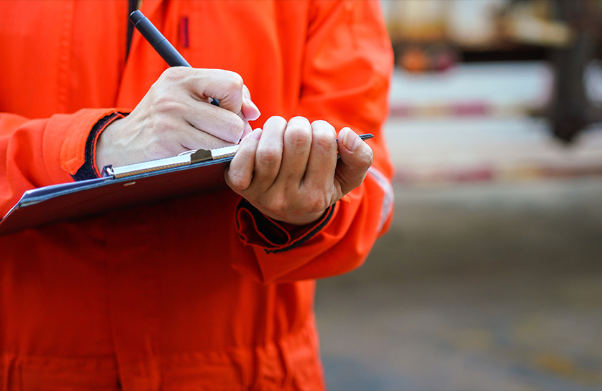 A person in an orange jumpsuit writing on a clipboard