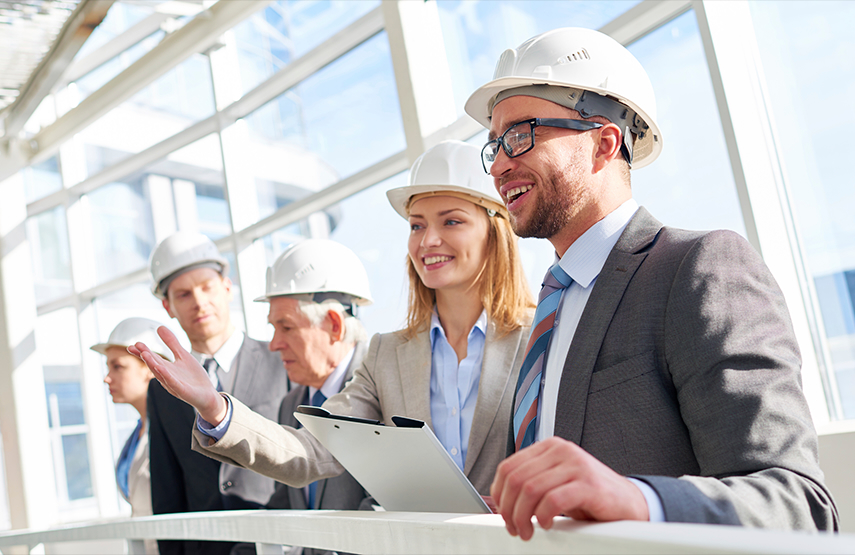 A group of people in suits and hard hats, pointing and smiling at something out of the frame